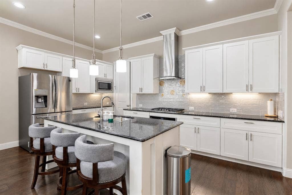 1603 Coventry Court, Farmers Branch, TX 75234 Kitchen featuring white cabinetry, dark stone countertops, stainless steel appliances, a center island with pendant lighting, and wood-finish flooring