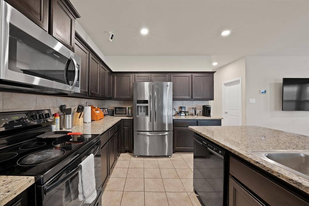228 Foxhunter Street, Fort Worth, TX 76131 Kitchen featuring dark wood cabinetry, light-toned granite countertops, stainless steel appliances, tile flooring, and recessed lighting