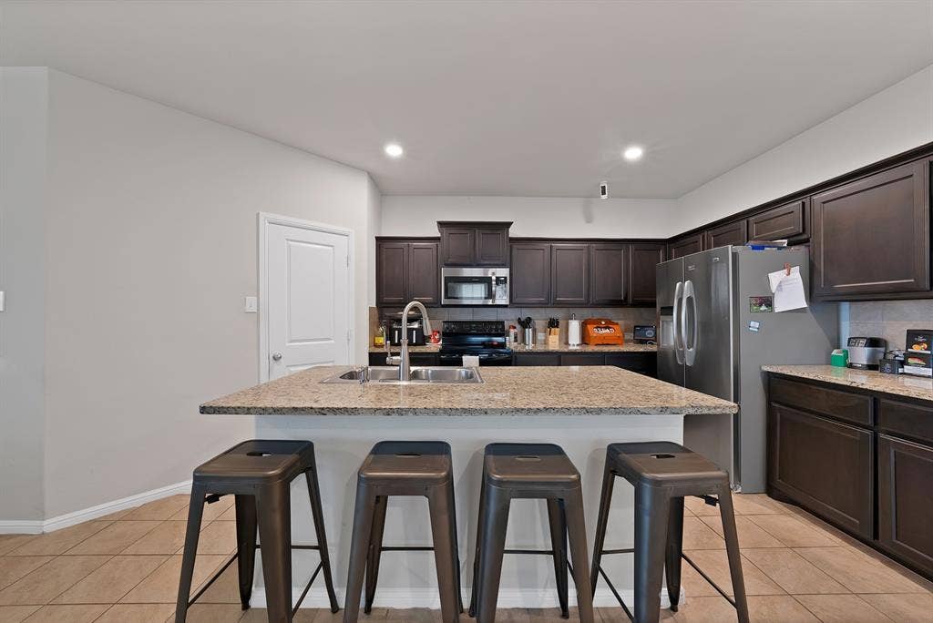228 Foxhunter Street, Fort Worth, TX 76131 Kitchen featuring a central island, dark wood-finish cabinetry, light-colored countertops, and tile flooring