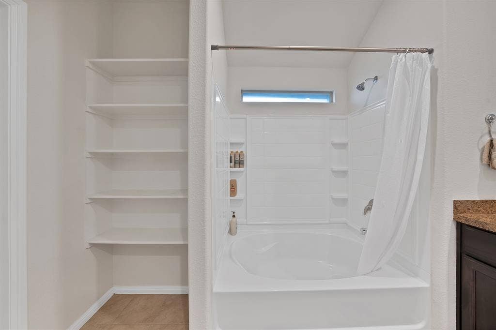 228 Foxhunter Street, Fort Worth, TX 76131 Built-in shelving, white bathtub with integrated shower, and a high-set horizontal window