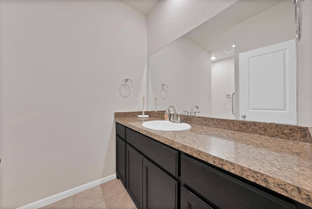228 Foxhunter Street, Fort Worth, TX 76131 Vanity with a polished countertop, integrated white sink, chrome faucet, and dark wood-finish cabinetry