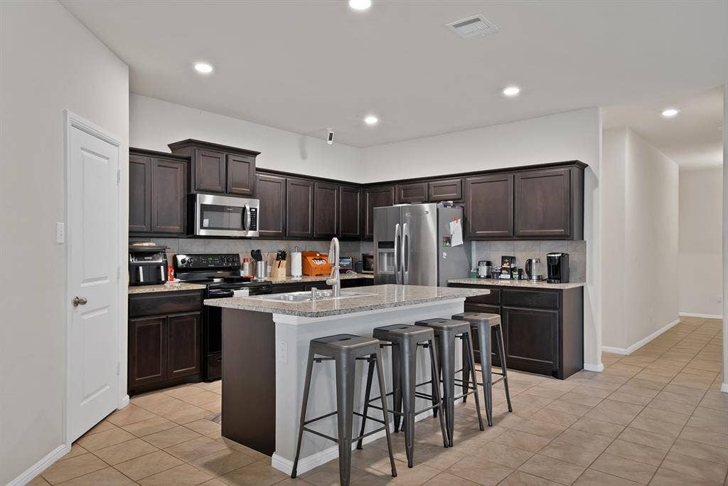 228 Foxhunter Street, Fort Worth, TX 76131 Kitchen featuring dark wood-finish cabinetry, stainless steel appliances, a center island with countertop seating, recessed lighting, and tile flooring