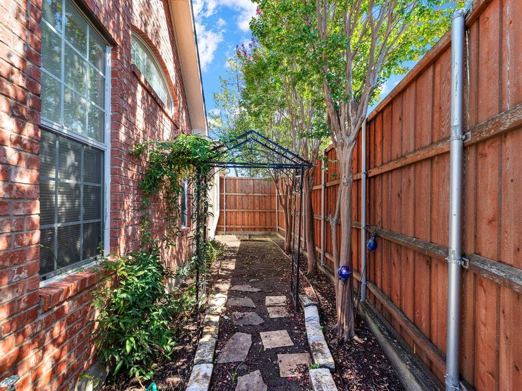 A stepping-stone path winds through the sheltered side garden, where mature crape myrtles filter sunlight beside tall windows. Take a peaceful morning pause to tend the greenery and enjoy a little time outdoors before your day begins.
