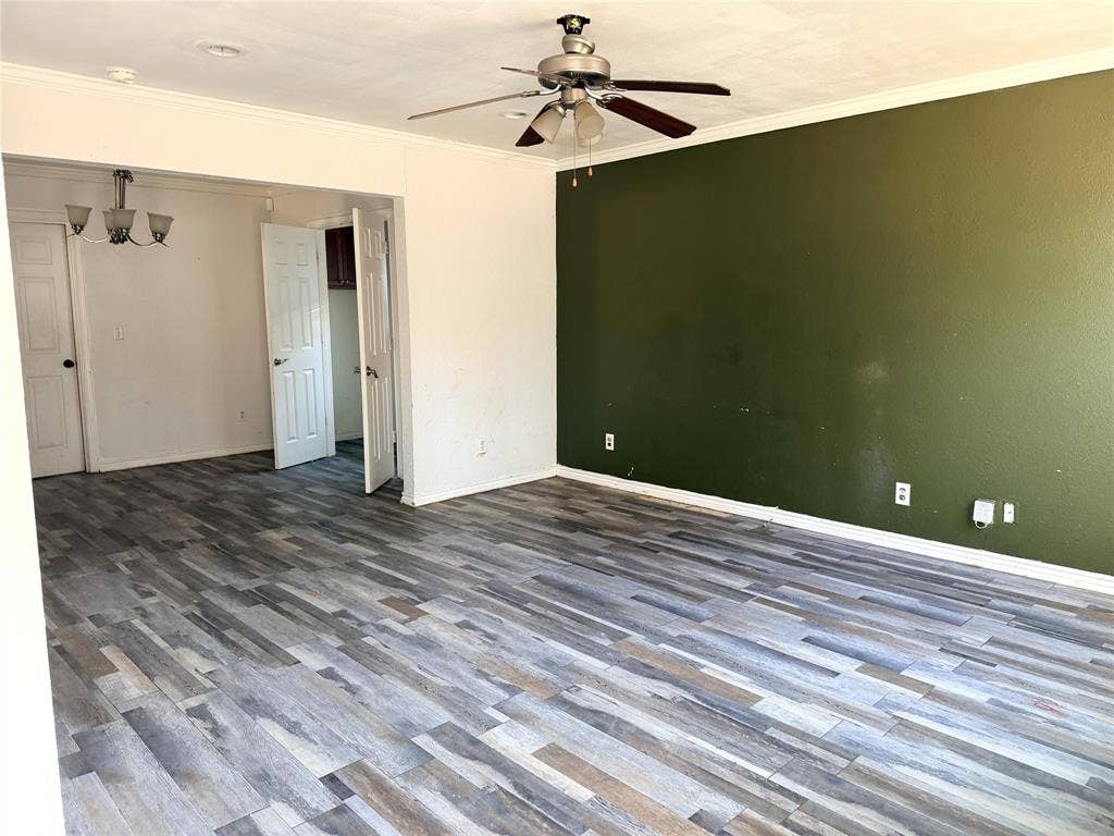 Wood-finish flooring throughout, ceiling fan with light fixture, white crown molding, and two panel doors