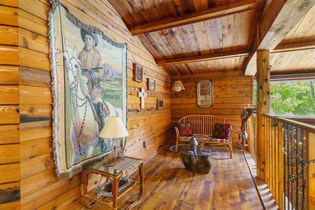 8685 FM 1827, Anna, TX 75409 Log-paneled walls and ceiling with exposed timber support beams, natural wood-finish flooring, and a decorative metal spindle railing