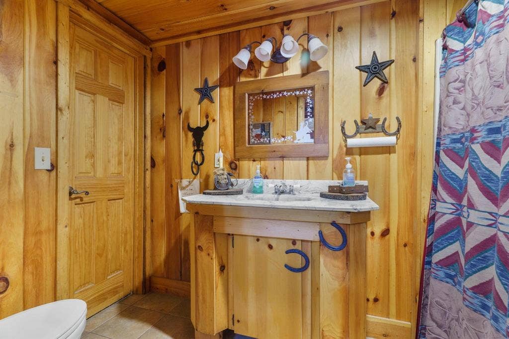 8685 FM 1827, Anna, TX 75409 Bathroom featuring vertical wood paneled walls, a custom wood vanity with a stone countertop, an integrated sink, a matching wood-framed mirror, and a four-light fixture