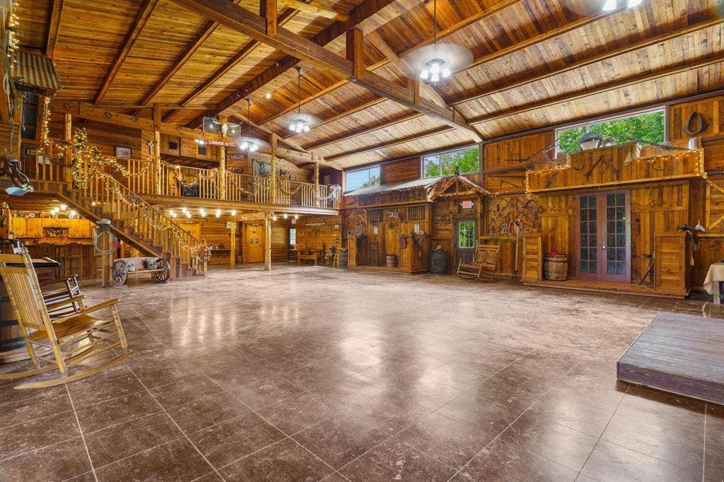 8685 FM 1827, Anna, TX 75409 Expansive open-concept interior featuring exposed wooden ceiling beams, natural wood wall paneling, tiled flooring, a built-in wooden staircase with matching railings, and glass-paneled double doors