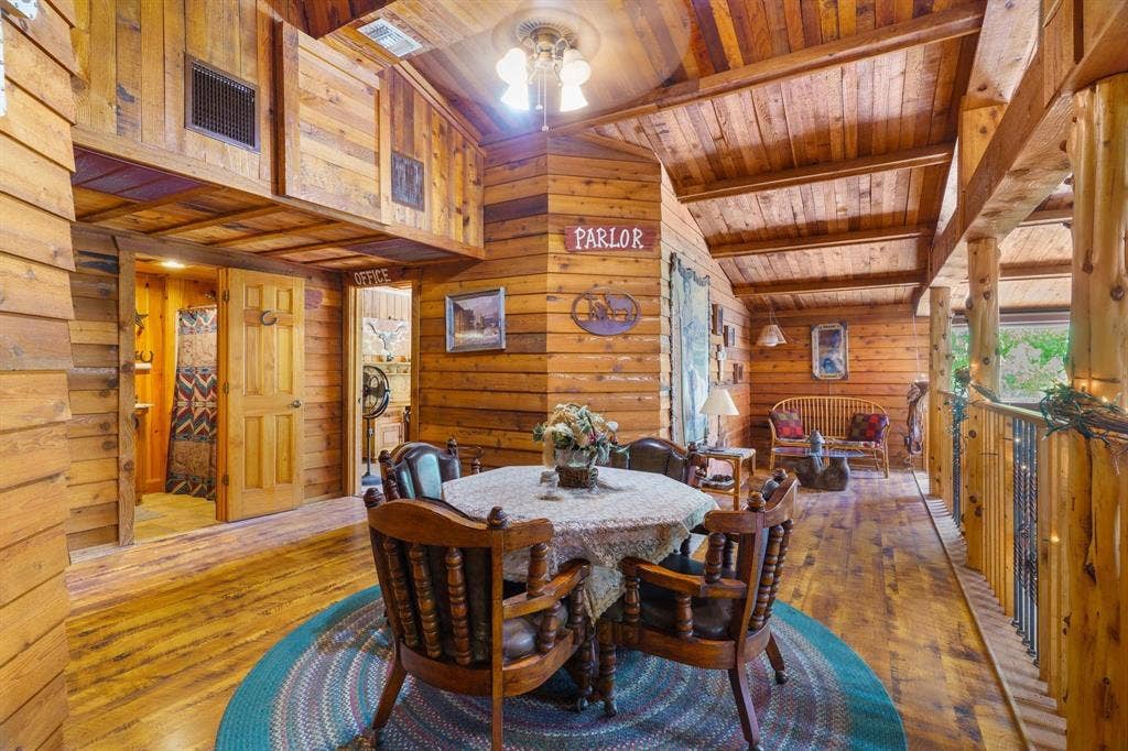 8685 FM 1827, Anna, TX 75409 Interior space featuring rustic log-style wall paneling, vaulted ceilings with exposed timber beams, wood-finish flooring, and a decorative metal railing