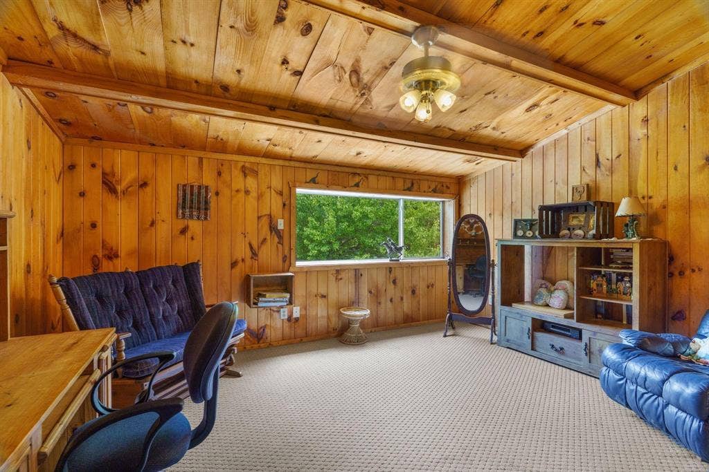 8685 FM 1827, Anna, TX 75409 Wood-paneled walls, vaulted ceiling with exposed wood beams, large picture window, and ceiling-mounted light fixture with frosted glass shades