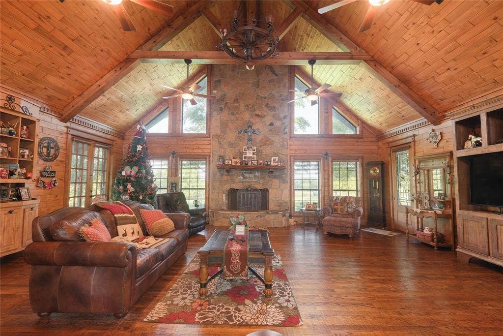 8685 FM 1827, Anna, TX 75409 Vaulted ceiling with exposed timber beams and wood-plank paneling, floor-to-ceiling stone fireplace, built-in cabinetry, wood-finish flooring, and multi-pane windows