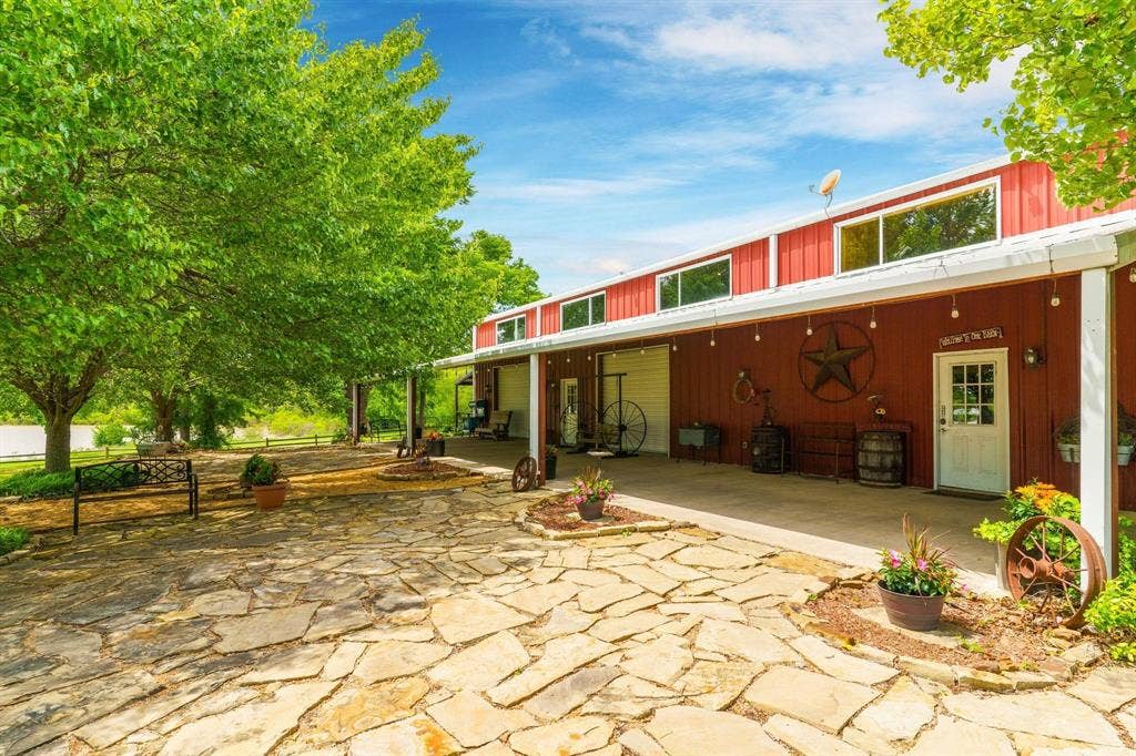 8685 FM 1827, Anna, TX 75409 Exterior featuring a red metal siding structure with a concrete patio, stone hardscaping, and a covered porch area