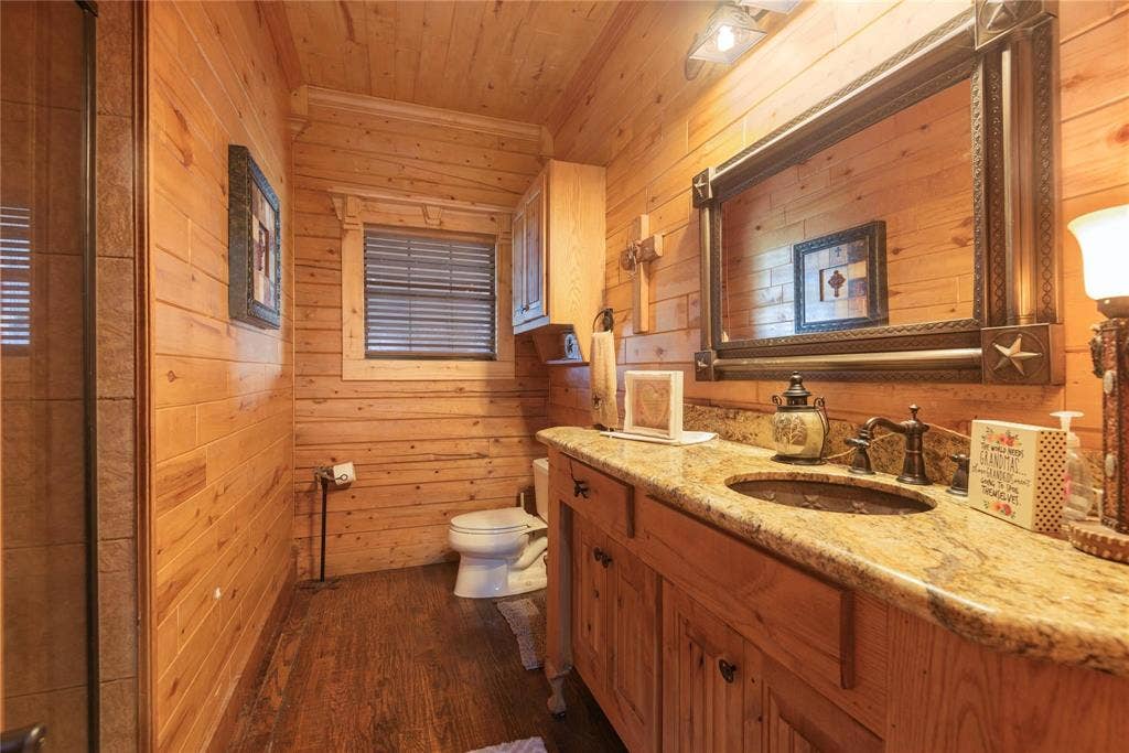 8685 FM 1827, Anna, TX 75409 Wood-paneled walls and ceiling, stone-finish vanity countertop with an integrated basin, custom wood cabinetry, and a large decorative wall-mounted mirror