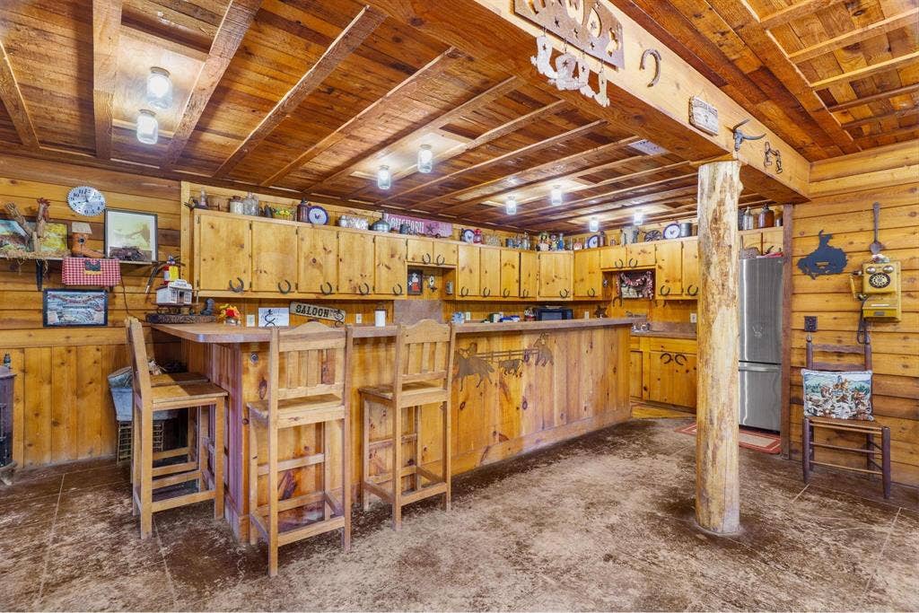 8685 FM 1827, Anna, TX 75409 Rustic bar area featuring knotty pine wall paneling, exposed beam ceiling, built-in wooden cabinetry, custom wood bar top, and a structural log pillar
