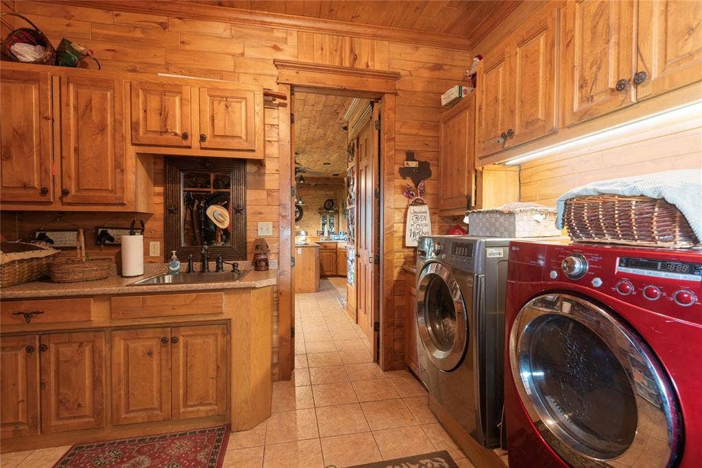 8685 FM 1827, Anna, TX 75409 Laundry room featuring knotty wood wall paneling, custom wood cabinetry, stone-finish countertops, an under-mount stainless steel sink with a bronze-finish faucet, and ceramic tile flooring