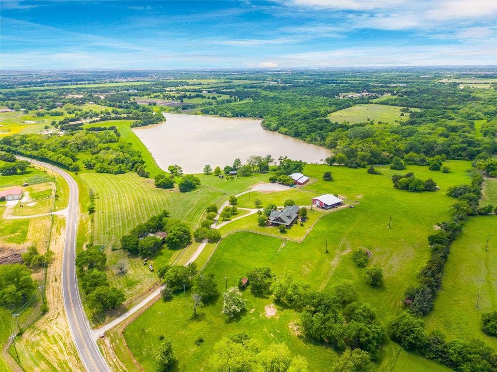 8685 FM 1827, Anna, TX 75409 Aerial perspective of acreage featuring a private pond, expansive green pastures, mature trees, and multiple outbuildings