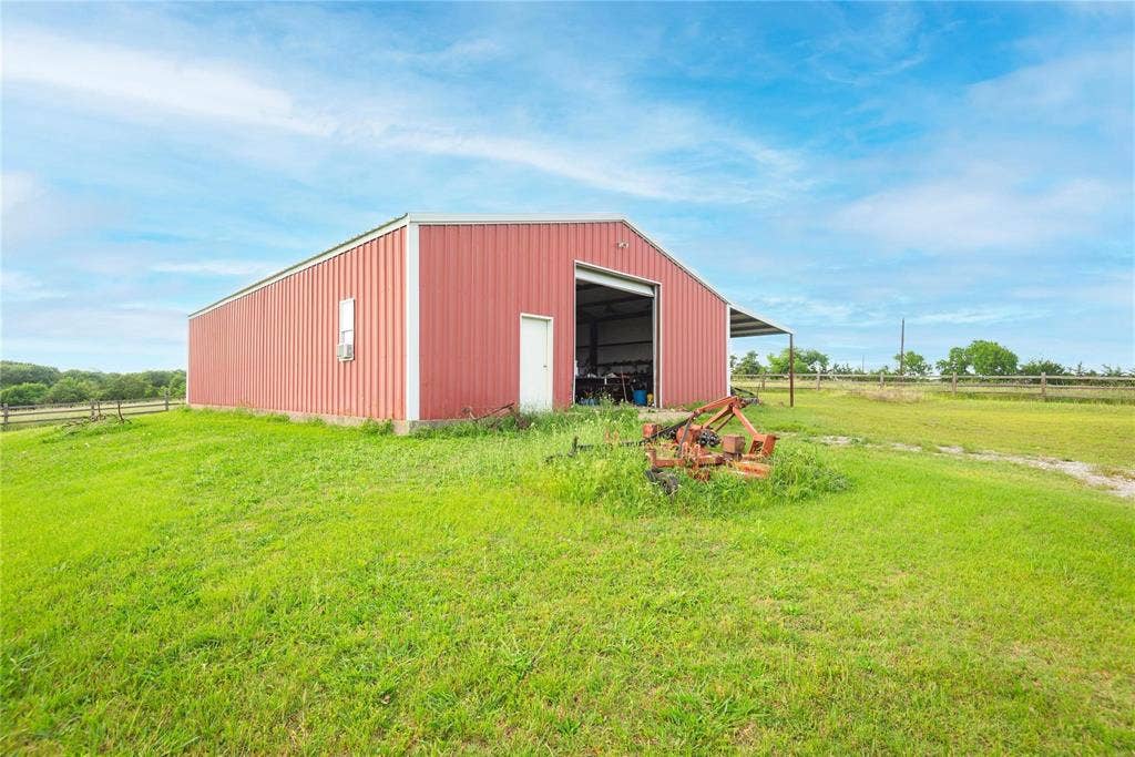 8685 FM 1827, Anna, TX 75409 Detached metal workshop featuring a gable roof, large sliding door, and open-sided lean-to structure situated on a grass lot