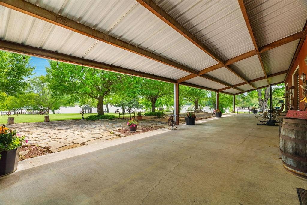 8685 FM 1827, Anna, TX 75409 Covered concrete patio featuring an exposed-beam ceiling with corrugated metal roofing, stone hardscaping, and mature trees