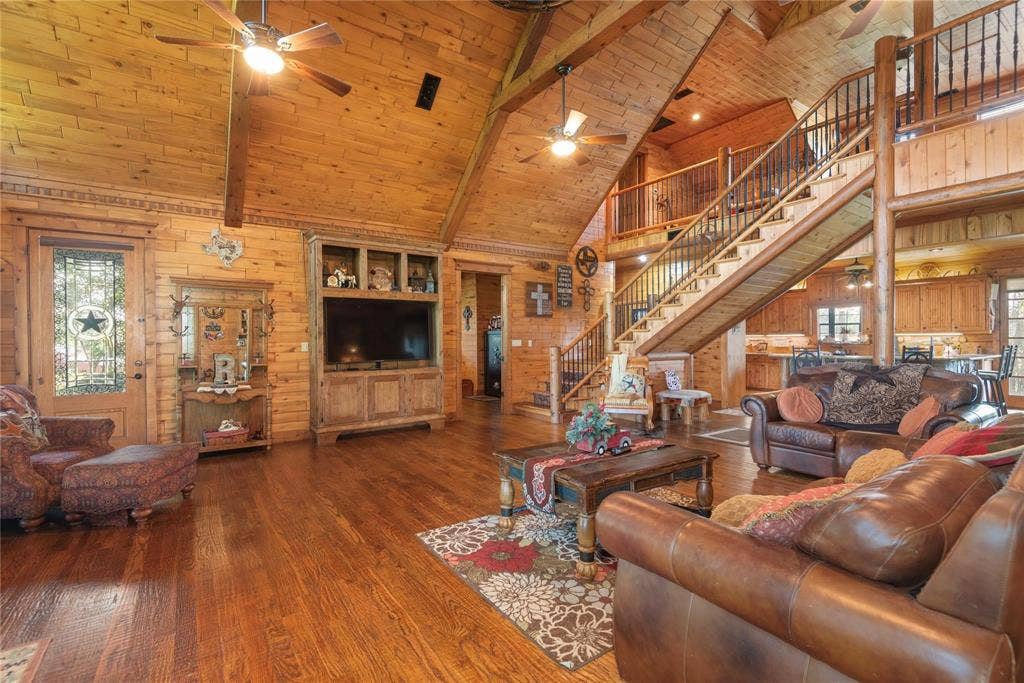 8685 FM 1827, Anna, TX 75409 Vaulted ceilings with exposed timber beams, wood-plank wall paneling, built-in media cabinetry, wood-finish flooring, and an open staircase featuring metal balusters