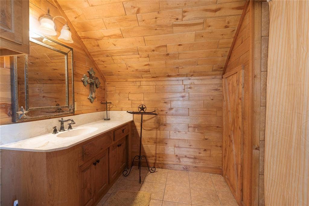 8685 FM 1827, Anna, TX 75409 Wood-paneled walls and ceiling, custom cabinetry vanity with an integrated basin, stone-surface countertop, and ceramic tile flooring