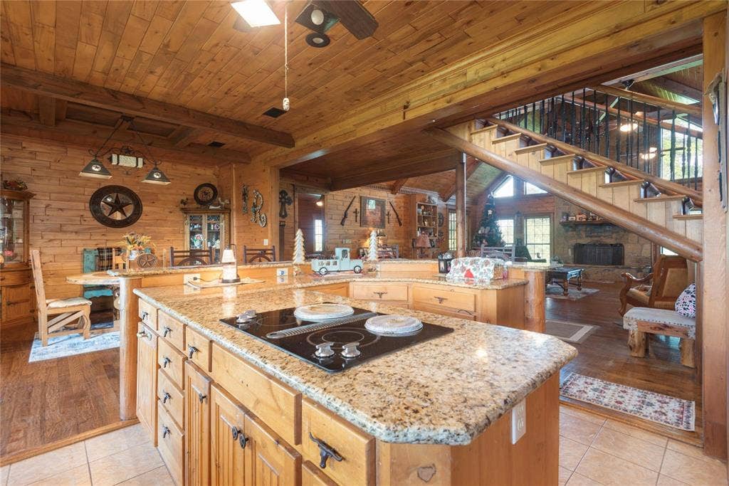 8685 FM 1827, Anna, TX 75409 Kitchen island featuring stone countertops, integrated cooktop, and wooden cabinetry, complemented by timber-plank wall paneling and an open staircase with decorative metal railing