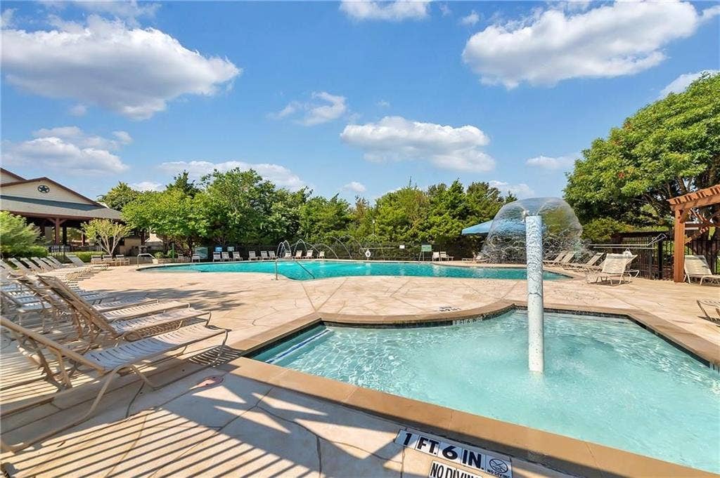 1545 Crystal Pass, Allen, TX 75002 Swimming pool with integrated spa and water feature, expansive paved decking, and lush surrounding landscaping