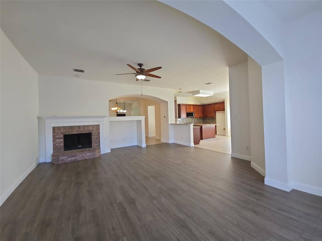 1545 Crystal Pass, Allen, TX 75002 Spacious interior with wood-finish flooring, a brick fireplace with white mantel, a ceiling fan, and arched openings