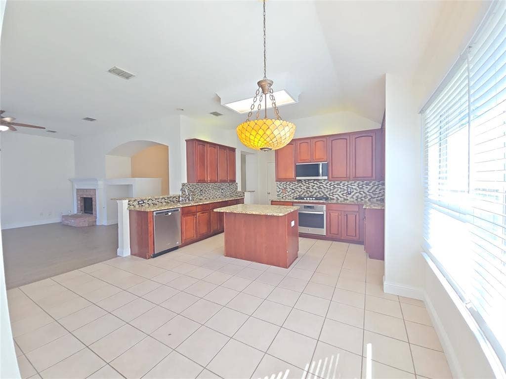 1545 Crystal Pass, Allen, TX 75002 Kitchen featuring an island, integrated stainless steel appliances, wood-finish cabinetry, and granite countertops