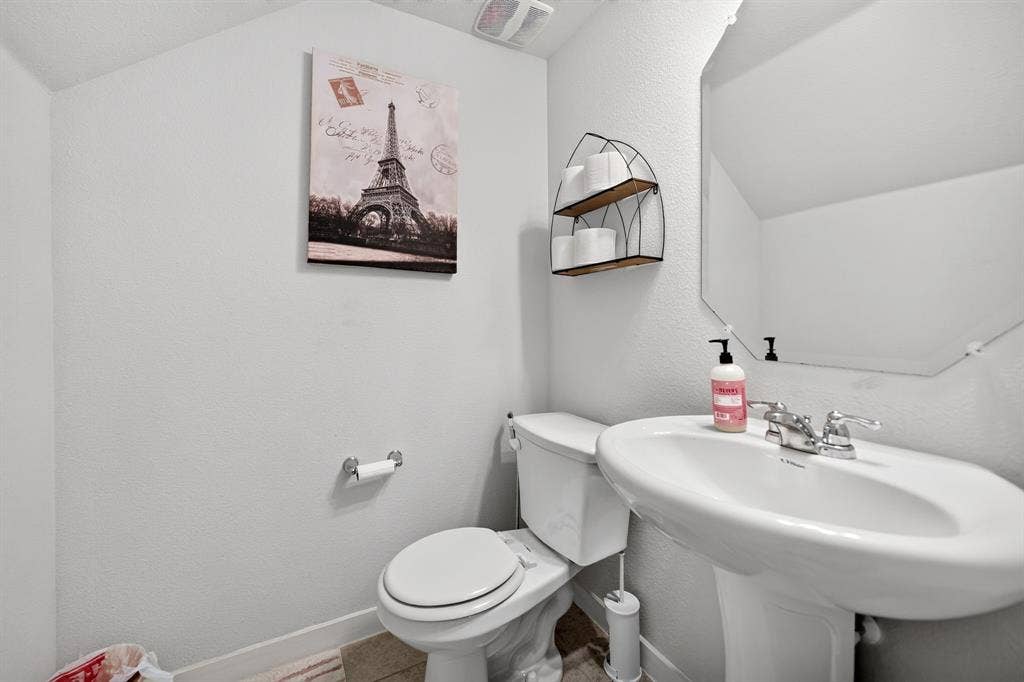 5534 Yarborough Drive, Forney, TX 75126 Pedestal sink with chrome faucet, toilet, wall-mounted mirror, and wall shelving