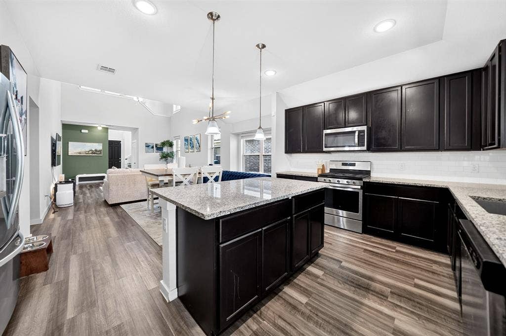 5534 Yarborough Drive, Forney, TX 75126 Open-concept kitchen featuring dark wood-finish cabinetry, light-toned granite countertops, a subway tile backsplash, stainless steel appliances, and wood-finish flooring