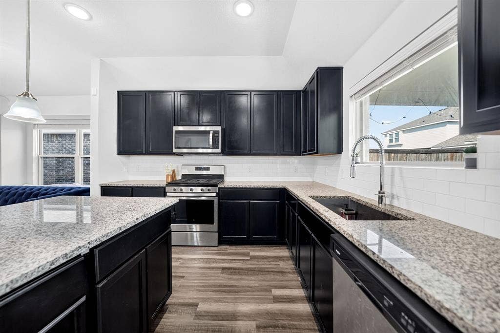 5534 Yarborough Drive, Forney, TX 75126 Kitchen featuring dark cabinetry, light-toned countertops, stainless steel appliances, a subway tile backsplash, and wood-finish flooring
