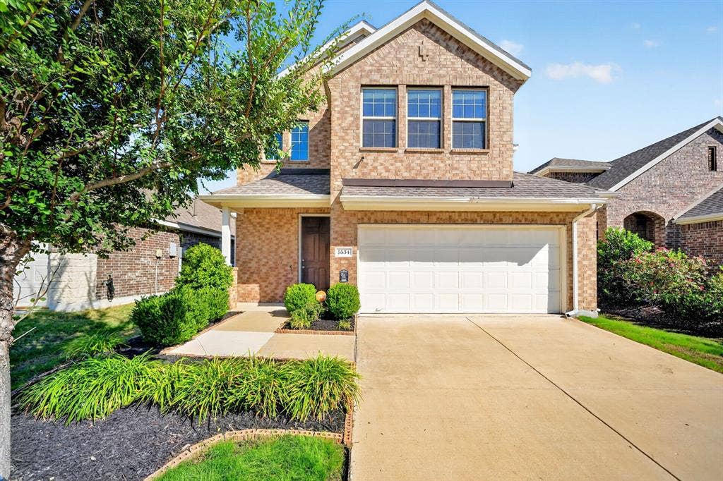 5534 Yarborough Drive, Forney, TX 75126 Charming brick two-story home featuring a clean concrete driveway, white garage door, and manicured front landscaping with ornamental grasses and mature greenery