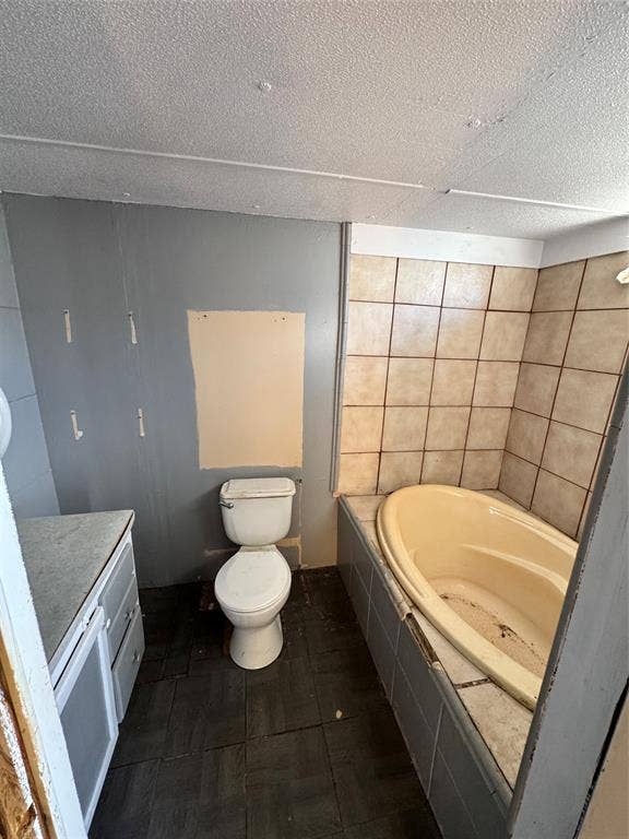 6624 Dayla Court, Granbury, TX 76049 Built-in bathtub with tiled surround, white toilet, vanity with integrated sink, and dark-toned floor tiles