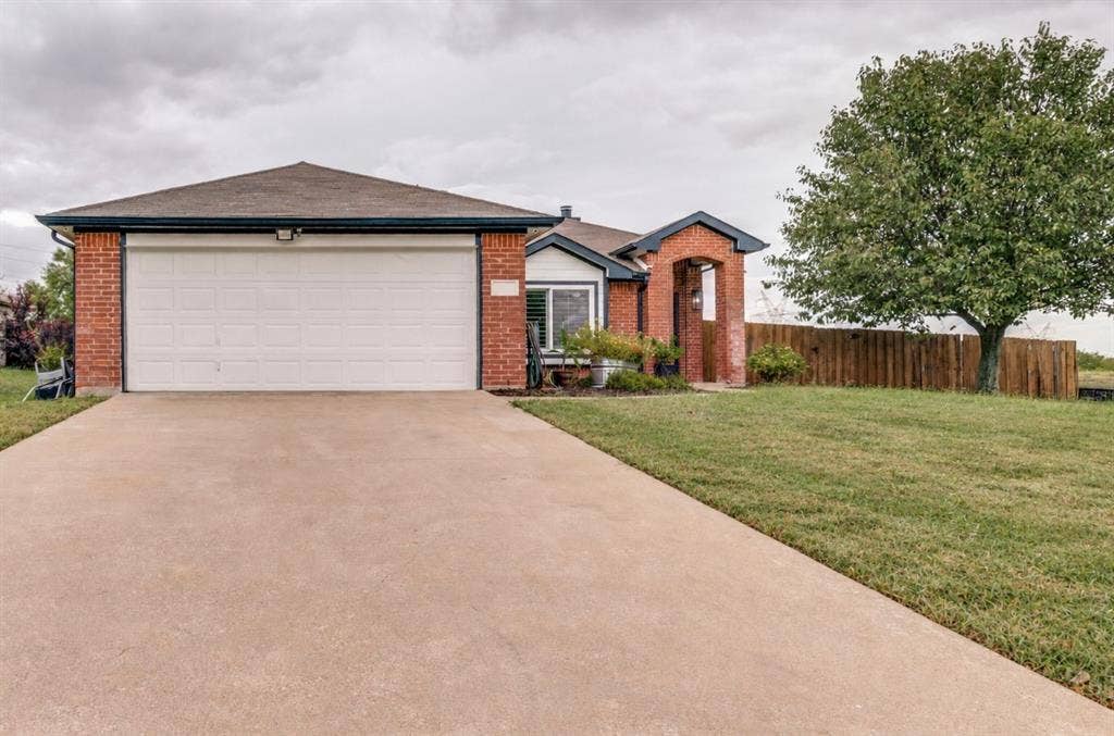 Brick exterior with a detached garage, expansive concrete driveway, and a mature tree