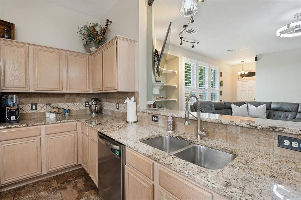 Kitchen featuring light wood cabinetry, stone countertops, a tile backsplash, and a double basin stainless steel sink