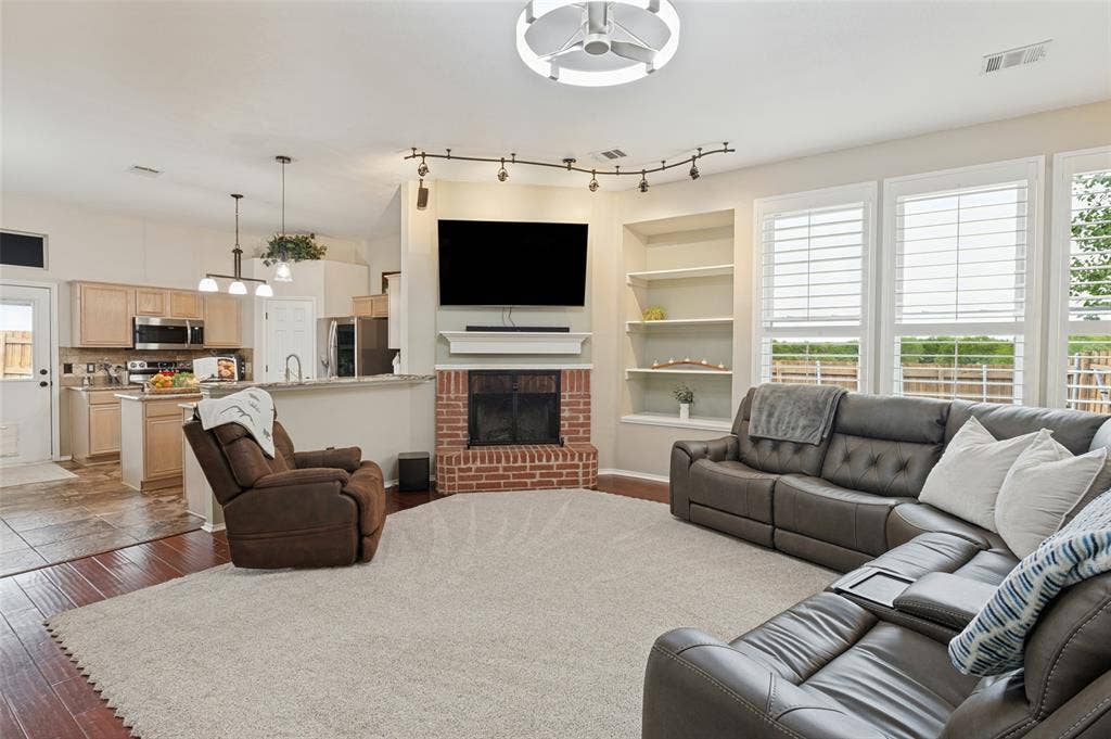 Spacious living area featuring a brick-surround fireplace, built-in shelving, and large windows with plantation shutters
