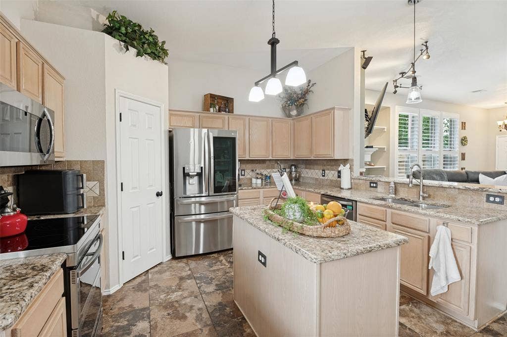 Kitchen featuring a central island, light wood-finish cabinetry, built-in stainless steel appliances, granite countertops, and tile flooring