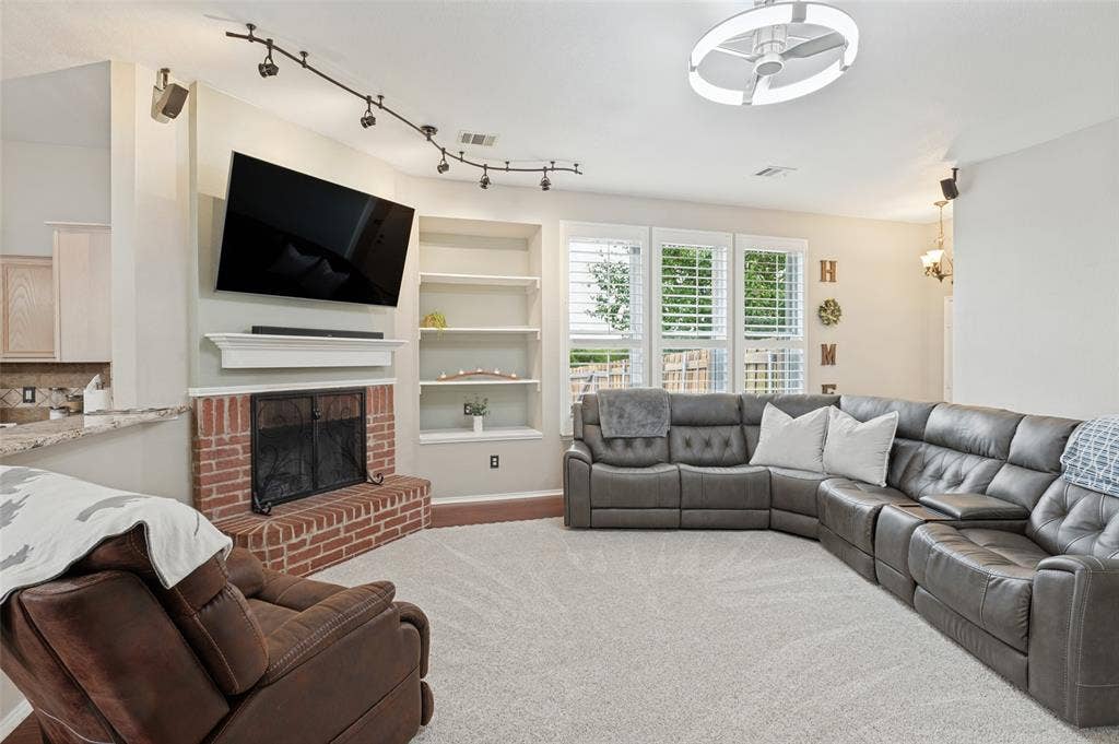 Recessed fireplace with a brick hearth, built-in shelving, track lighting, and multiple windows with plantation shutters