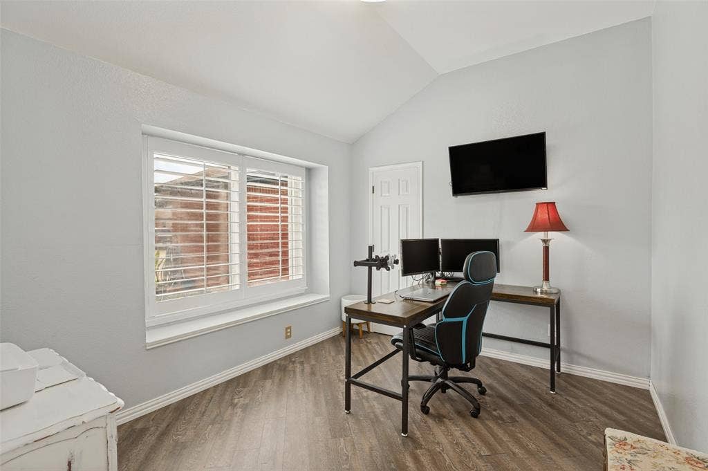 Vaulted ceiling, wood-finish flooring, white window shutters, light gray walls, and a white paneled door