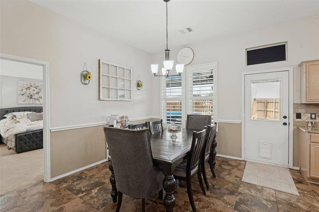 Dining area featuring durable tile flooring, a contemporary chandelier, white window shutters, and a white exterior door with glass paneling