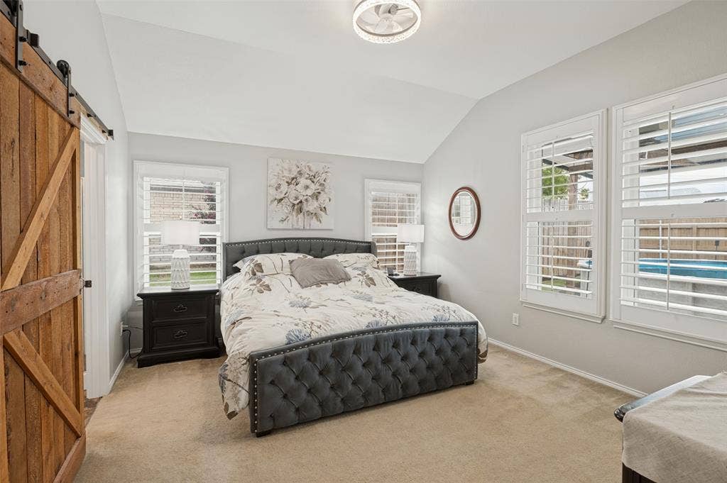 Vaulted ceiling, ceiling-mounted light fixture, three windows with plantation shutters, wood-finish barn door, carpeted flooring