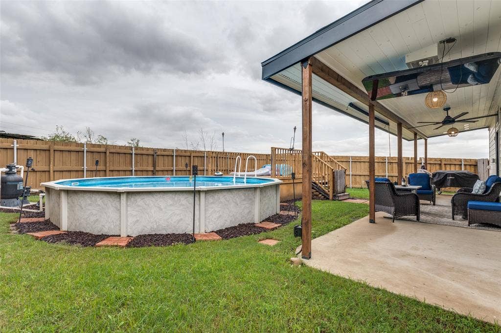 Expansive concrete patio with wood-post pergola, dual ceiling fans, and an above-ground pool