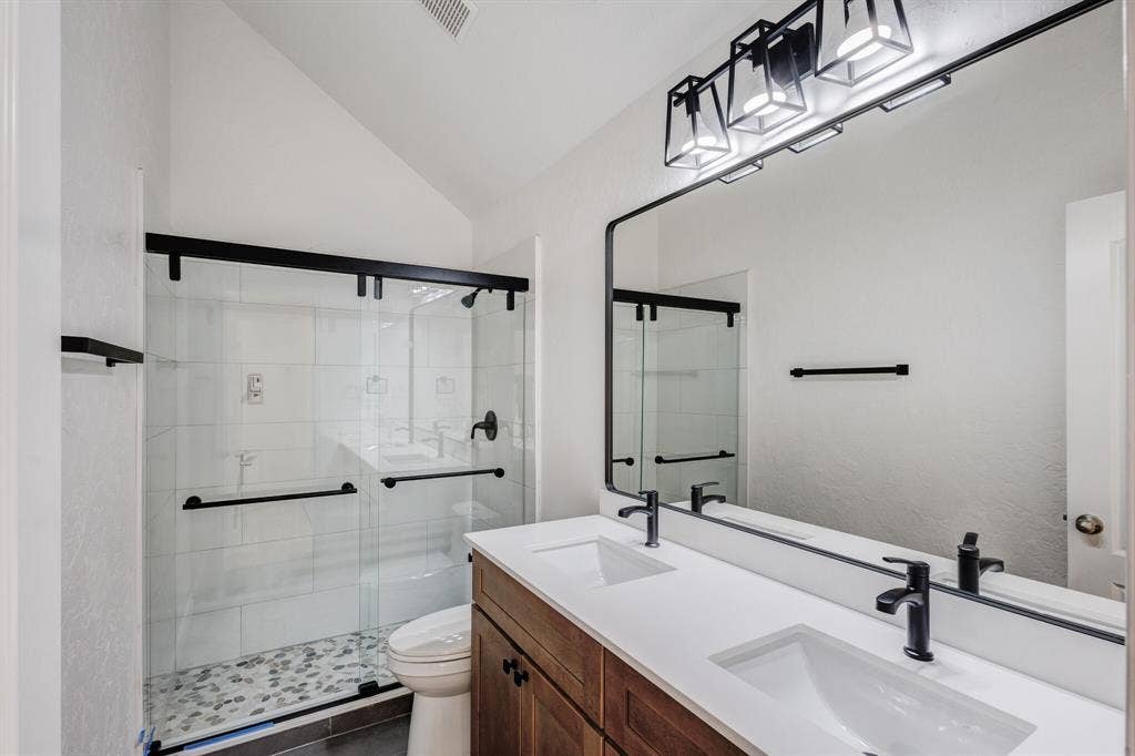 1306 Bentley Drive, Carrollton, TX 75006 Bathroom with a shower with door, vaulted ceiling, double vanity, tile patterned floors, and toilet
