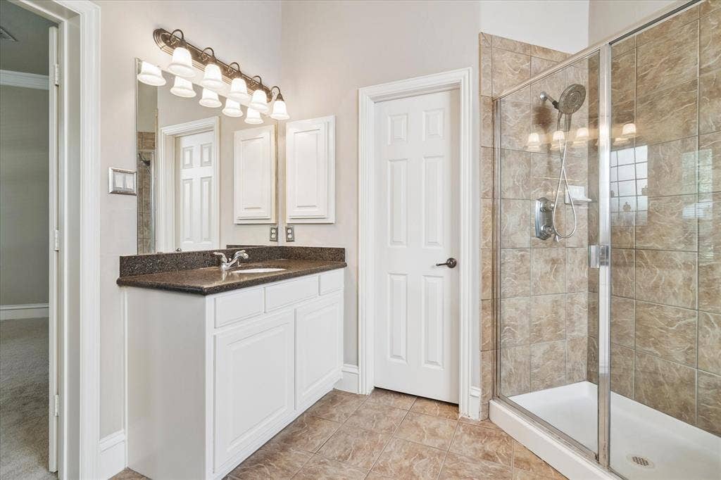 8323 Albritton Drive, Frisco, TX 75036 Glass-enclosed shower with tiled walls, white vanity with a dark countertop, integrated sink, and overhead lighting fixture