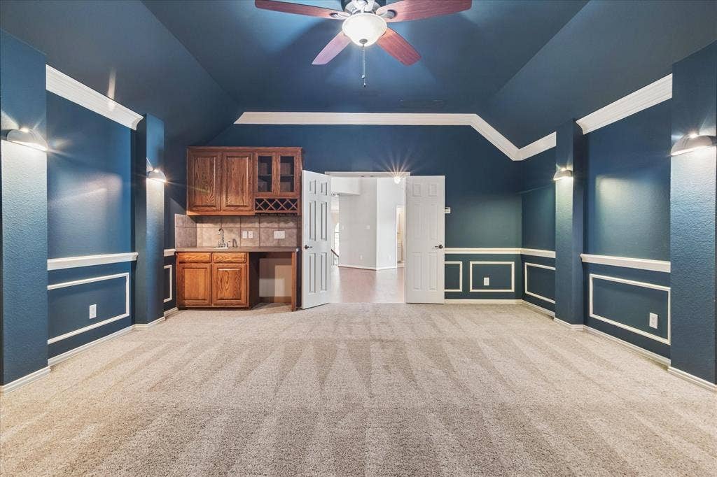 8323 Albritton Drive, Frisco, TX 75036 Built-in wet bar with wood cabinetry and tile backsplash, ceiling fan with light fixture, recessed wall paneling, and wall-mounted sconces