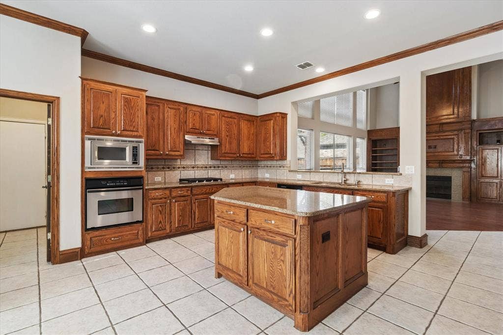 8323 Albritton Drive, Frisco, TX 75036 Kitchen featuring wood cabinetry, stainless steel appliances, a center island with a stone countertop, tile flooring, and recessed lighting