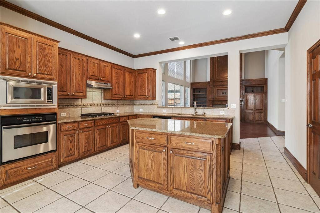 8323 Albritton Drive, Frisco, TX 75036 Kitchen featuring wood cabinetry, stainless steel appliances, a center island with a stone-finish countertop, and tile flooring