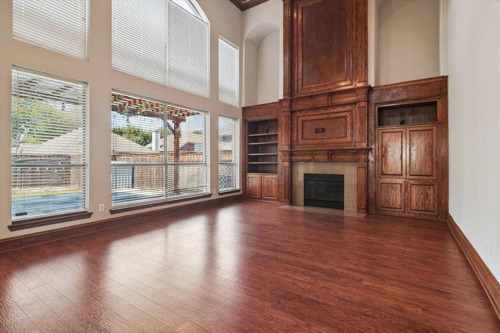 8323 Albritton Drive, Frisco, TX 75036 Expansive living space featuring wood-finish flooring, a full-height decorative wood mantel with built-in cabinetry, and a fireplace with a stone surround