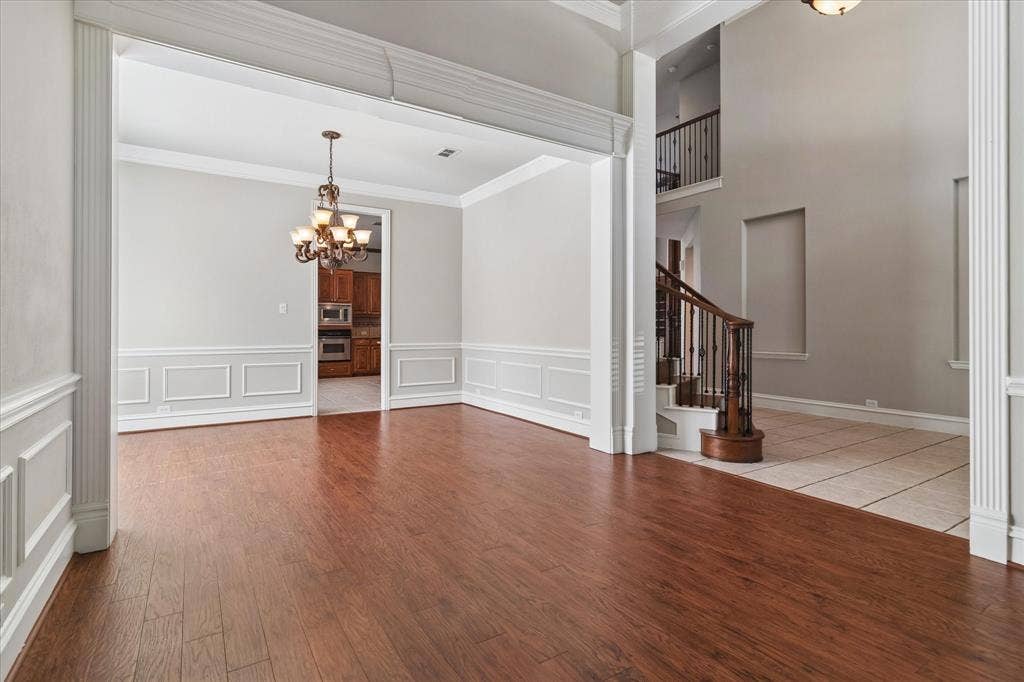 8323 Albritton Drive, Frisco, TX 75036 Hardwood-finish flooring, decorative wainscoting, chandelier lighting, arched entryway, and a grand staircase with dark wood railings