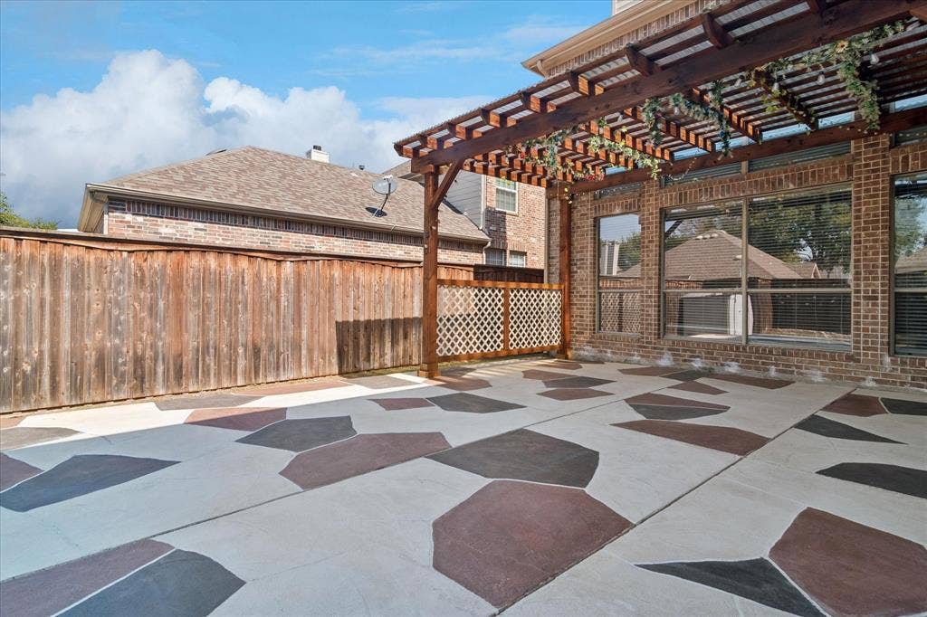8323 Albritton Drive, Frisco, TX 75036 Expansive patio with decorative patterned concrete flooring, a wood pergola structure, and a brick exterior wall with multiple windows