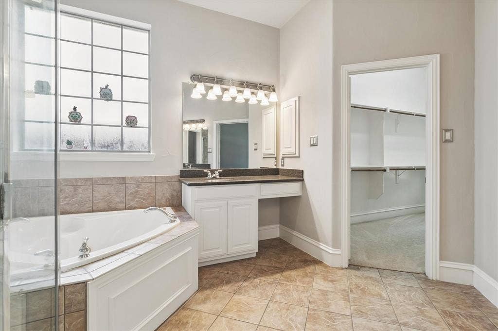 8323 Albritton Drive, Frisco, TX 75036 Corner soaking tub with tiled surround, adjacent glass-enclosed shower, dual vanity with undermount sinks, and separate water closet